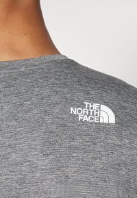 Camisa gris de manga corta con una textura jaspeada, que presenta un logo blanco de "The North Face" en la parte superior izquierda.