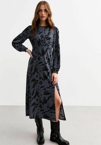 Langes, dunkelgraues Kleid mit schwarzen abstrakten Mustern, verfügt über lange Ärmel, eine taillierte Taille und einen seitlichen Schlitz, kombiniert mit schwarzen Knöchelstiefeln.