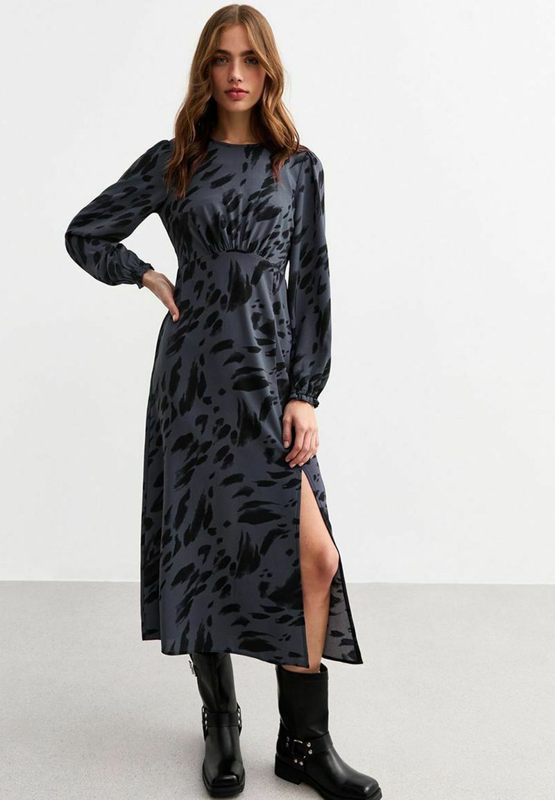 Langes, dunkelgraues Kleid mit schwarzen abstrakten Mustern, verfügt über lange Ärmel, eine taillierte Taille und einen seitlichen Schlitz, kombiniert mit schwarzen Knöchelstiefeln.