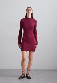 Burgundy pitkähiha dressi, istuva muotoilu, polven ylle ulottuva pituus, sileä rakenne. Yhdistetty mustiin nauhakenkiin, minimalistinen tausta.