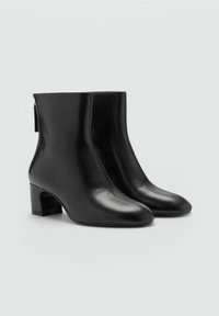 Bottes noires en cuir montantes avec un bout pointu, un talon bloc moyen et un design minimaliste. Présentant une texture lisse et une silhouette élégante.