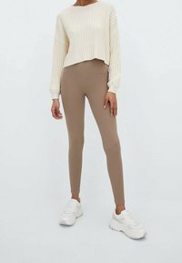 Jersey de canalé crema con mangas anchas combinado con leggings de canalé beige y zapatillas blancas con sutiles acentos grises.
