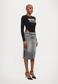 Top de manga longa preto com textura canelada e texto "Moschino Jeans"; saia midi em denim cinza ajustada com fendas laterais, combinada com sapatos de salto alto pretos.