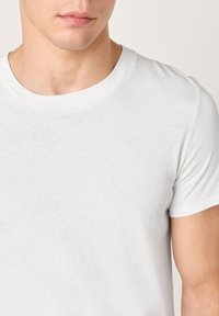 T-shirt bianca in cotone con scollo rotondo classico e maniche corte, caratterizzata da una texture discreta e una finitura liscia.