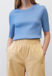Světle modrý žebrovaný top s krátkým rukávem a kulatým výstřihem, spárovaný s vysokými žlutými kalhotami, které mají boční kapsy a strukturovanou látku.