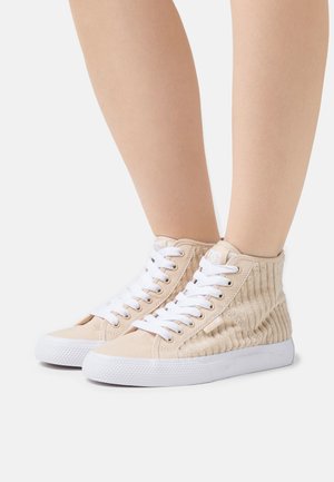 Zapatillas altas de tela beige con paneles acanalados texturizados, cordones blancos, punta redonda y suela de goma. Diseño simple sin acentos adicionales.