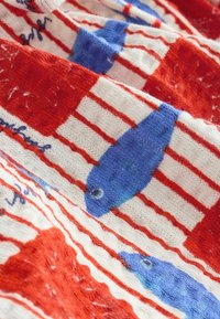 Tissu à rayures rouges et blanches avec des motifs de poissons bleus et une petite écriture bleu foncé, montrant la texture tricotée en gros plan.