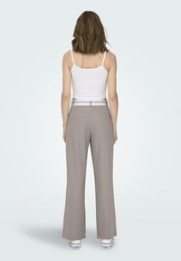 Pantalones de pierna ancha grises con una textura suave, que cuentan con un cinturón blanco. Llevados con una camiseta ajustada blanca y zapatillas blancas.