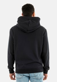 Zwarte hoodie met een ruime capuchon en geribde manchetten. Beschikt over een zachte textuur en een eenvoudig ontwerp, gedragen met lichtblauwe jeans.
