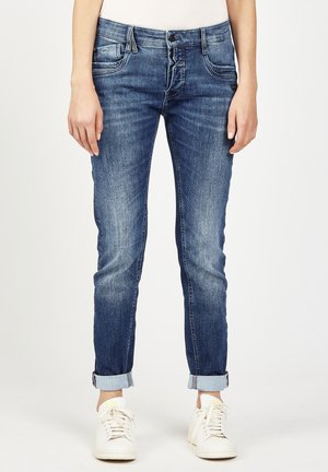 Skinny jeans made of blue denim, featuring a faded wash, five-pocket design, and rolled cuffs. Paired with white sneakers.