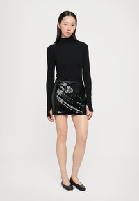 Top negru cu guler înalt, asociat cu o fustă mini neagră cu paiete, având un design ajustat și o textură netedă. Purtați cu pantofi planși negri.
