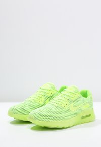Pair of neon green Nike Air Max sneakers with mesh upper and visible air cushioning on white surface.
