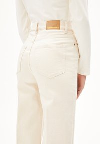 Beige denim jeans met een hoge taille, met een leren label met "ARMEDANGELS," twee achterzakken en zichtbare stiksels.