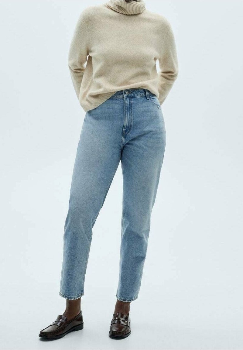 Jean bleu clair taille haute à coupe droite, en denim. Associé à un pull col roulé beige ; des mocassins marron complètent le look.