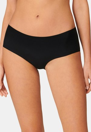 Frau trägt nahtlose schwarze Hipster-Unterwäsche, angeschnittener Bauch und obere Oberschenkel sind vor weißem Hintergrund sichtbar.