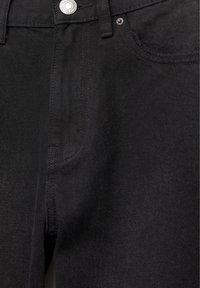 Gros plan sur le devant d'un jean en denim noir montrant le bouton, la zone de la fermeture éclair, les passants de ceinture et les détails des poches.