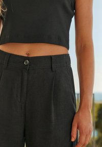 Mustad linased püksid eesnööbiga kinnitamisega, küljetaskutega ja sirge jala disainiga. Õmmeldud kärbitud musta ribaga topiga.
