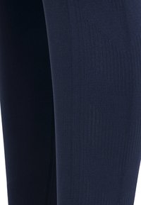 Close-up van donkerblauwe geribbelde textielstof met verticaal breipatroon, waarbij de textuur en stiksel details worden benadrukt.