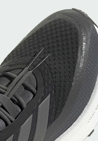 Chaussure de sport noire avec une tige texturée, des accents lisses et des détails réfléchissants. Comprend une semelle en caoutchouc grise avec une finition à motif.