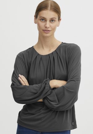 Blusa gris de manga larga con frente plisado, corte relajado y puños fruncidos. Tejido suave y liso; escote redondo con un detalle sutil de logo.