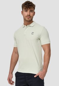 Helles grünes Poloshirt mit weicher Textur, versehen mit einem kleinen navy Logo und einem klassischen Kragen. Kurzarm-Design und gerader Saum.