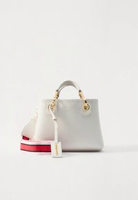 Sac à main en cuir blanc avec ferrures dorées, double poignée supérieure et une bandoulière rayée amovible en rouge et rose. Comprend une étiquette suspendue.