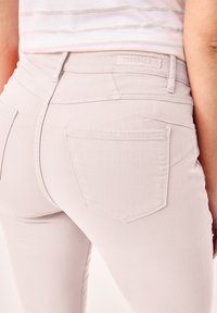 Helle rosa Denim-Jeans mit glatter Textur, ausgestattet mit einem standardmäßigen Rückentaschendesign und subtilen Nähdetails. Das Etikett von Paddock ist sichtbar.