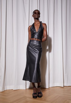 Top halter de couro preto e saia midi com corte evasê, textura suave, design ajustado, com sandálias plataforma a condizer, contra um fundo claro.