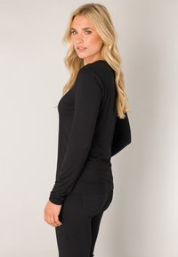 Zwart top met lange mouwen van zacht materiaal, voorzien van een aansluitend ontwerp en een ronde hals, gecombineerd met bijpassende zwarte aansluitende broek.