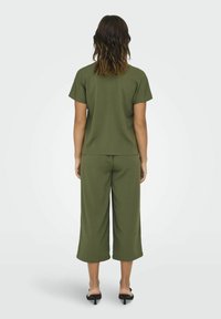 Conjunto verde oliva que incluye una blusa de manga corta y pantalones cortos, hecho de material suave con un ajuste holgado y diseño de pierna ancha.