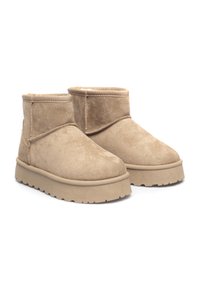 Beżowe zamszowe botki za kostkę z okrągłym noskiem, grubą teksturowaną podeszwą oraz przeszyciami na wierzchu. Miękka podszewka widoczna przy kołnierzu.