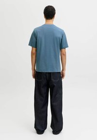 Camiseta azul de algodón con mangas cortas y cuello redondo; combinada con vaqueros de mezclilla oscuros de corte holgado, con bolsillos traseros y costuras visibles.