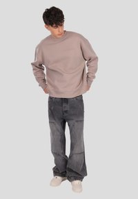 Svetlo taupe majica z okroglim izrezom in vezenim napisom, v kombinaciji s širokimi temno sivimi jeans hlačami z uničenimi detajli in šivi.