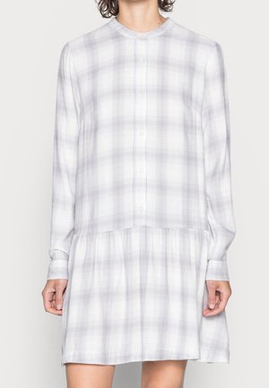 Kobieta w długiej, zapinanej na guziki sukience w jasnoszarą kratę, z marszczonym dołem i okrągłym dekoltem.