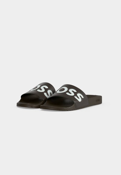 Paire de sandales slides noires avec un logo blanc en gras "BOSS" sur les brides, semelles intérieures texturées et semelles plates sur fond gris clair.