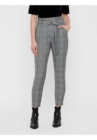 Pantalon à carreaux gris à taille haute, ceinture à nouer, coupe effilée et texture subtile. Associé à des bottines noires.