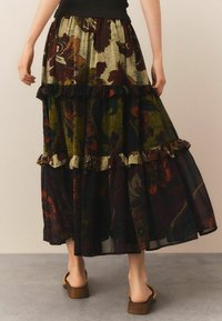 Fustă lungă, în straturi, cu un model floral în verde închis, burgundy și crem, cu margini fâlfâitoare și o secțiune superioară ajustată de culoare neagră.