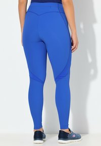 Niebieskie legginsy sportowe o gładkiej fakturze, z kontrastującymi wzorami szwów. Połączone z ciemnymi, wzorzystymi sneakersami dla kontrastu.