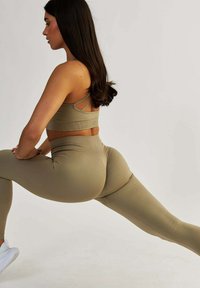Beige sportovní podprsenka a legíny s vysokým pasem vyrobené z elastického materiálu. Podprsenka má tenké ramínka; legíny mají bezšvový design a decentní logo.
