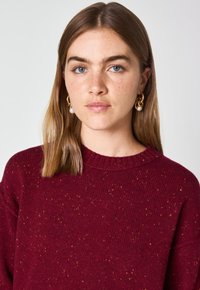 Maglione a maglia bordeaux con collo rotondo, caratterizzato da un motivo testurizzato e sottili riflessi dorati, realizzato in un materiale morbido.
