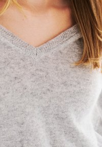 Grijze v-hals trui van zacht materiaal met een gestructureerde brei. De stof heeft een subtiel gesprenkeld patroon, wat het knusse uiterlijk benadrukt.