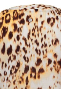Tela de estampado de leopardo con tonos de crema, marrón y amarillo. Textura suave, con un pequeño emblema metálico de marca en la parte posterior.