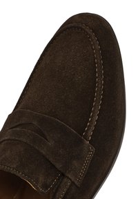 Brown suede loafers with a textured finish, featuring a stitched accent and a decorative strap across the top. Rounded toe and flexible sole.