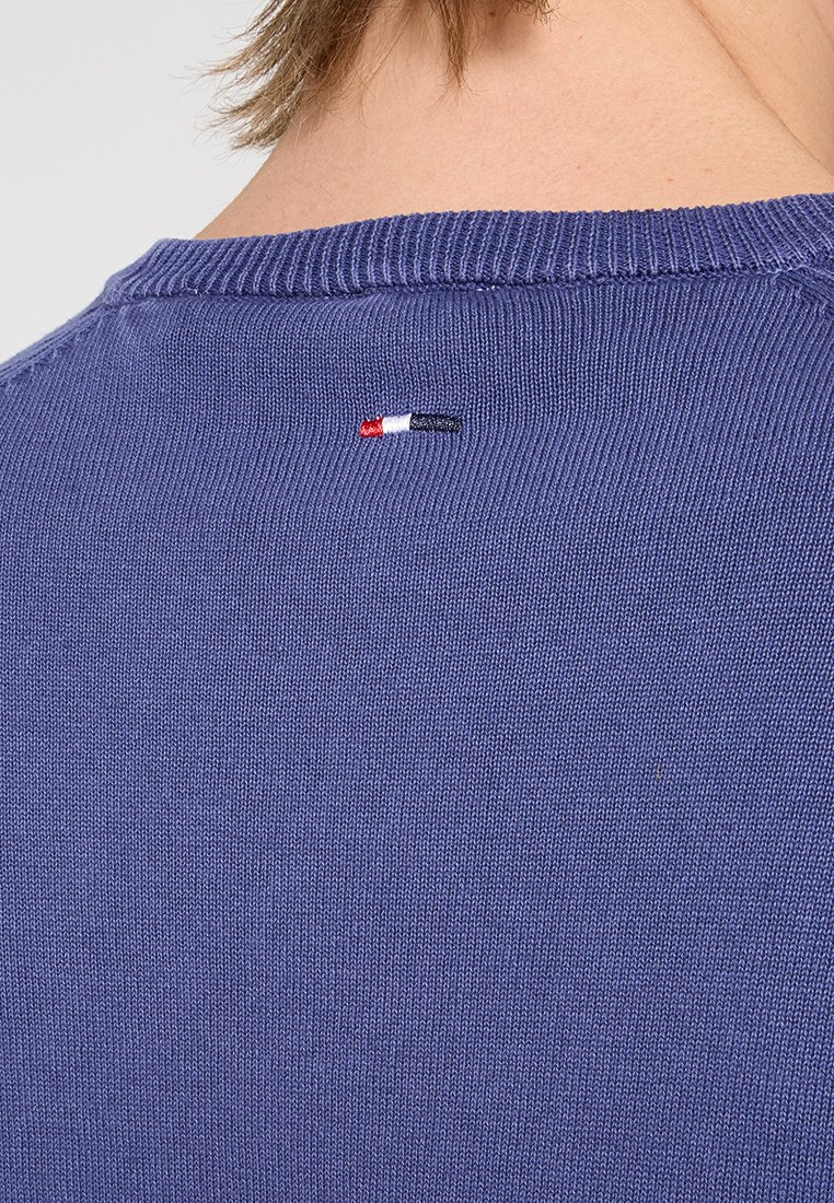 Granatowy sweter dzianinowy z okrągłym dekoltem. Posiada małe haftowane logo w czerwonym, białym i niebieskim kolorze na plecach w pobliżu szyi.