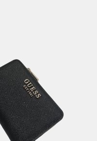 Portafoglio nero con texture, dotato di hardware argentato, presenta il logo "GUESS" e una chiusura a zip liscia su un lato.