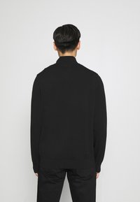 Pulover negru tricotat cu guler înalt și mansete cu nervuri, având un design curat și minimalist. Materialul pare neted și moale.