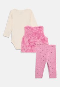 Completo a tre pezzi: body a maniche lunghe color crema, gilet fluffy rosa e leggings rosa con pois neri. Materiali morbidi e texture varie.