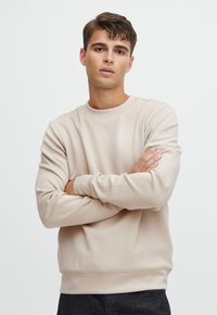 Beige crewneck sweatshirt made of soft fabric, featuring long sleeves and a relaxed fit. Smooth texture with ribbed cuffs and hem.