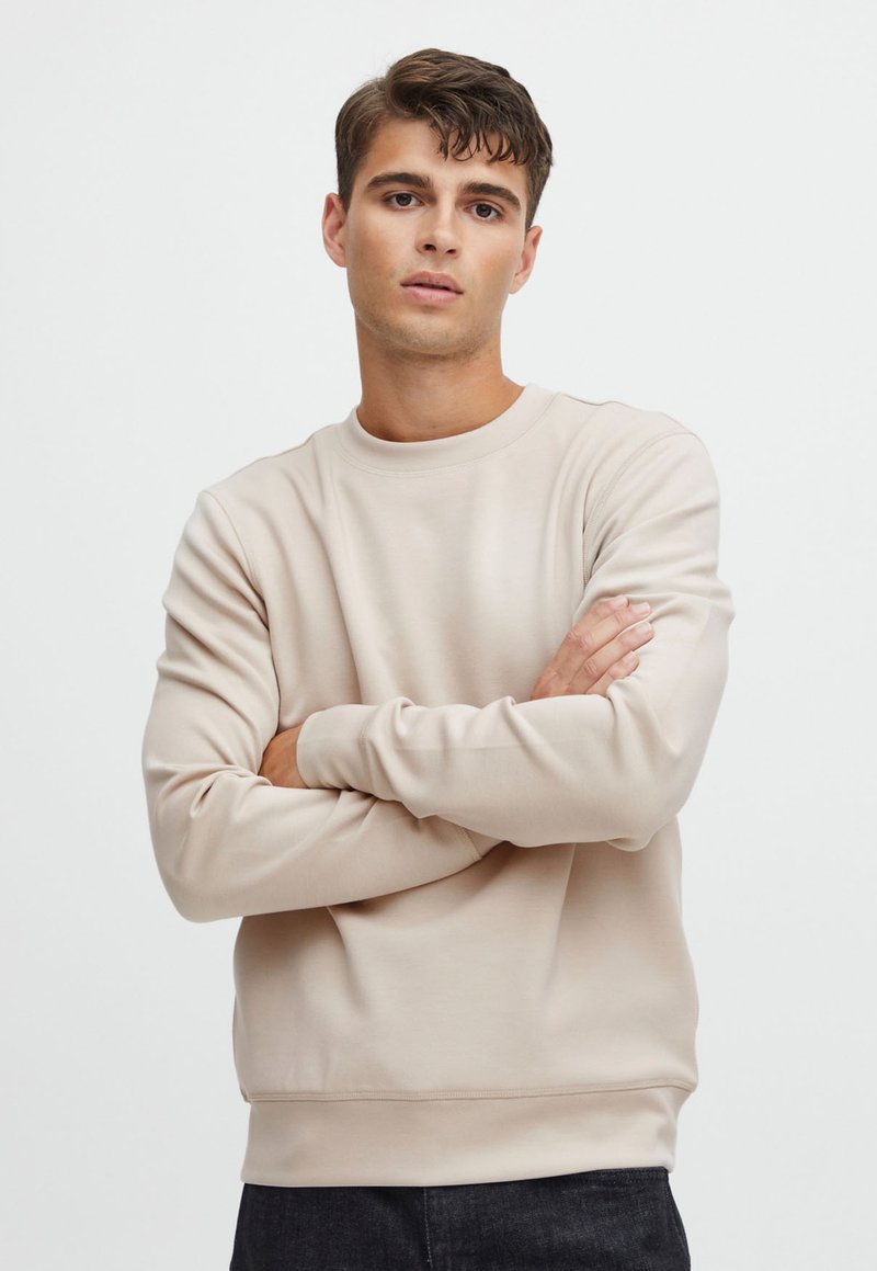 Beige crewneck sweatshirt made of soft fabric, featuring long sleeves and a relaxed fit. Smooth texture with ribbed cuffs and hem.