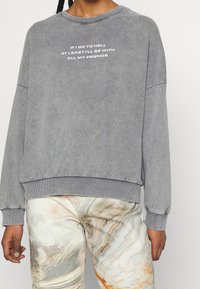 Szara bluza o luźnym kroju, z prążkowanymi ściągaczami na rękawach i dole, z białym napisem: "JEŚLI TRAFIAŁBYM DO PIEKŁA, PRZYNAJMNIEJ BYŁBYM ZE WSZYSTKIMI MOIMI PRZYJACIÓŁMI."